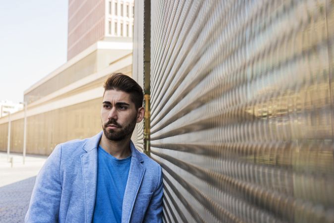 Young bearded man leaning on a wall and looking at camera and looking aside