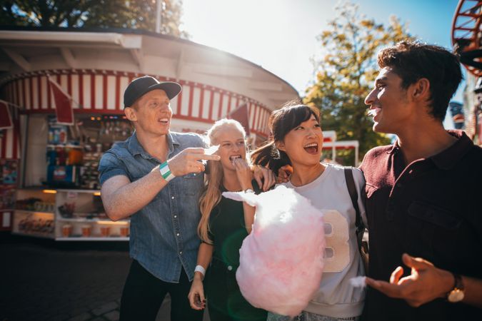 Group of friends having fun while eating cotton candy at fairground