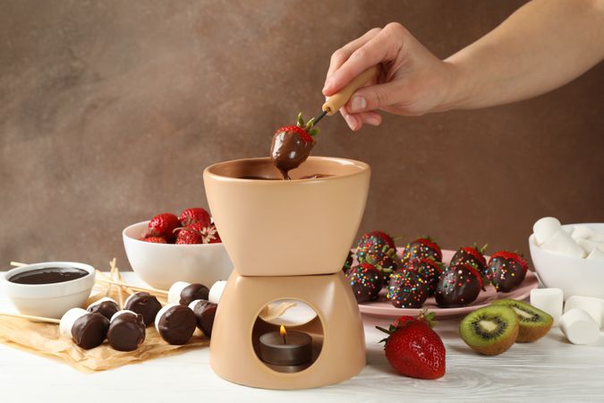 Woman dipping strawberry in chocolate. Delicious chocolate fondue