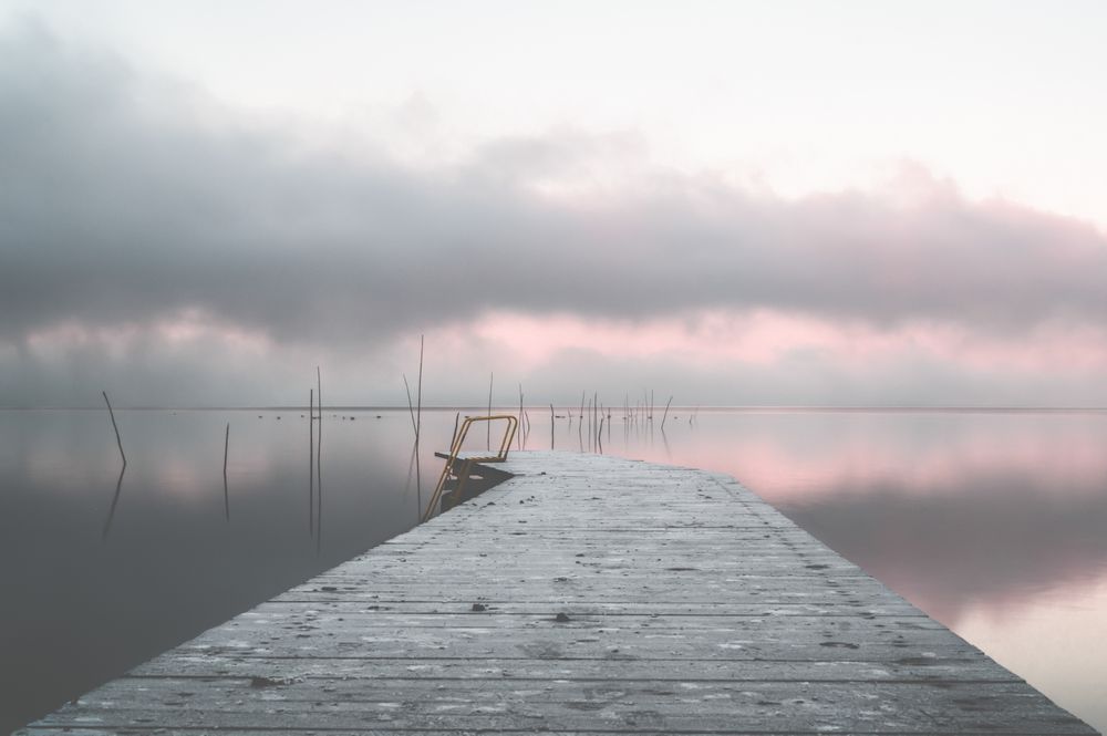 Light wooden dock on still sea under clouds