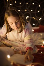 Girl reading book in bedroom decorated with Christmas lights