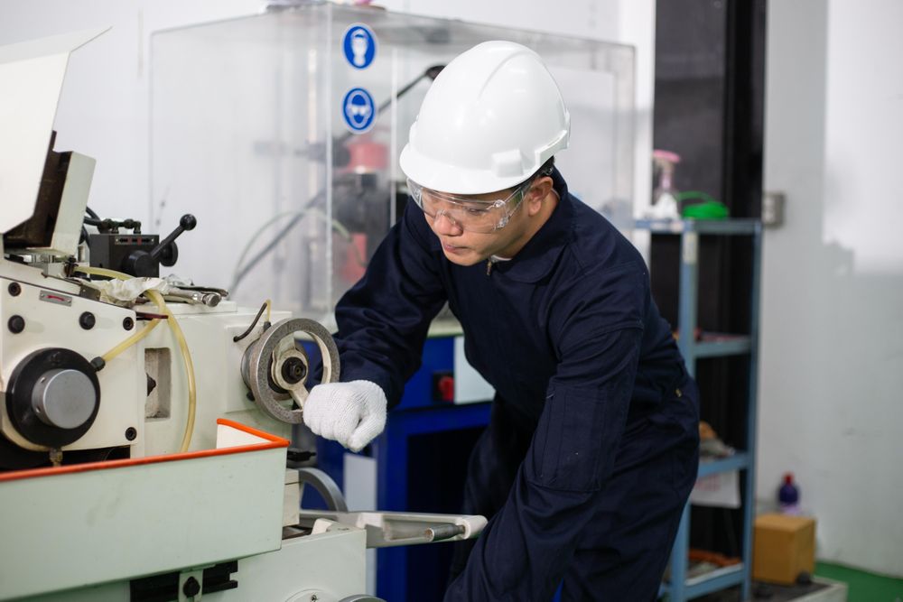 Man in hard hat and coveralls operating machine in factory