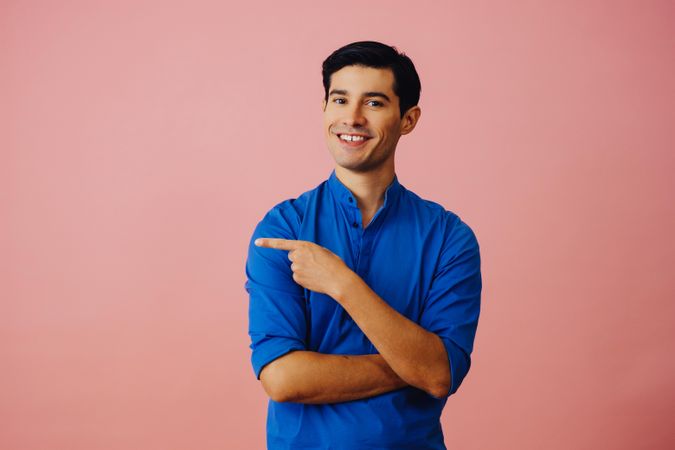 Medium shot of Latino man in pink studio with finger pointed to the left