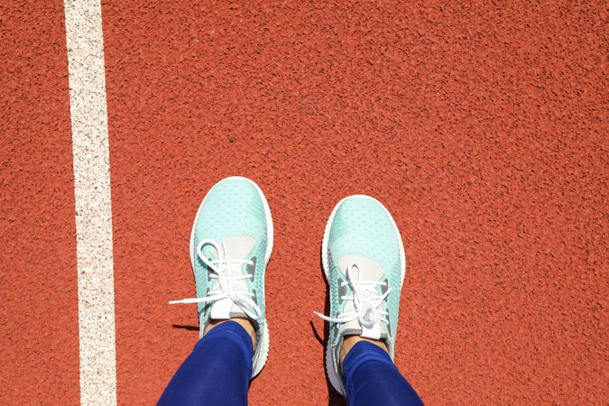 Female legs in sneakers on red athletic track background, space for text