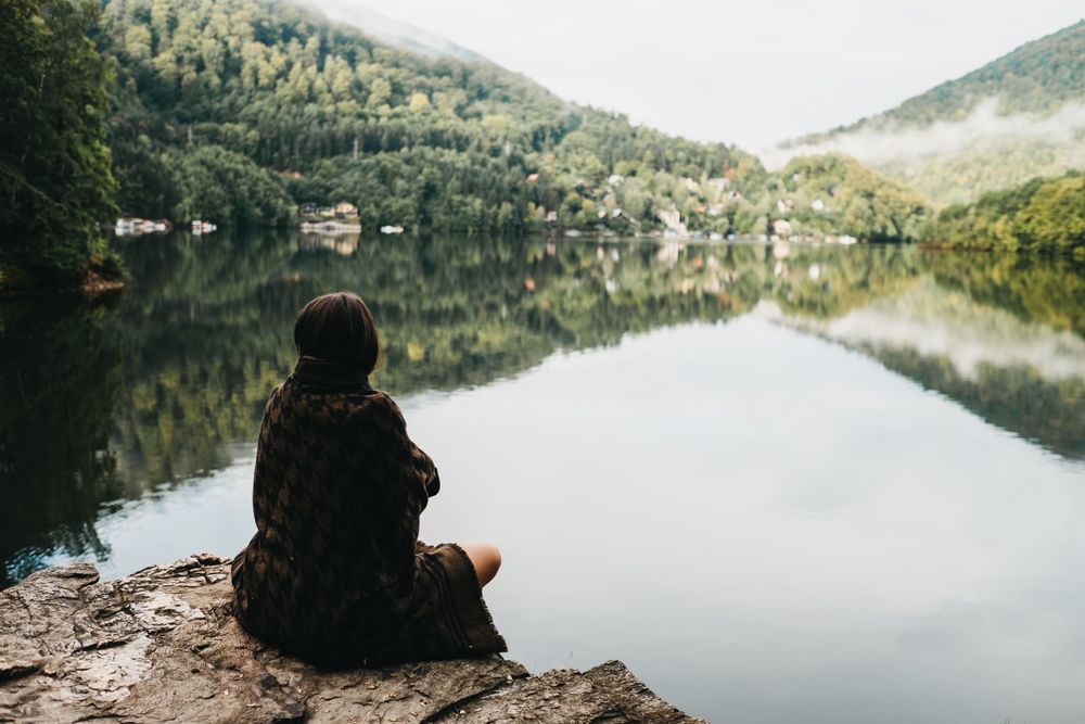 Woman sitting with blanket near lake and mountains