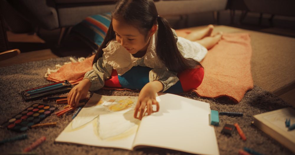 Evening Portrait of Cute Little Girl Drawing while Lying on the Floor in Living Room.