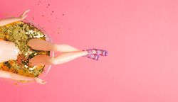 Top view of doll bathing in martini glass full of gold glitter on pink background