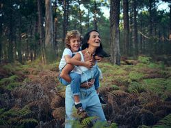 Son riding back of mother during walk in woods