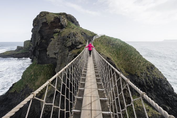 Woman crossing rope bridge leading to rocky island