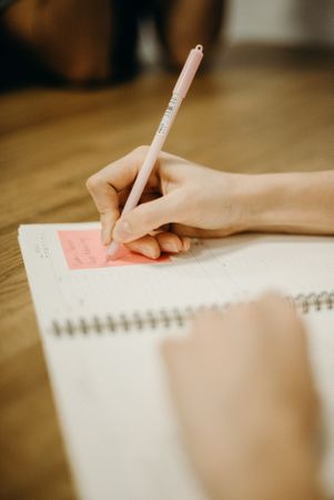 Cropped image of person writing on sticky note on notebook