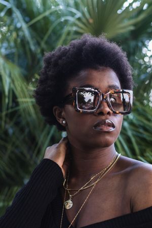 Confident Black woman in sunglasses against greenery