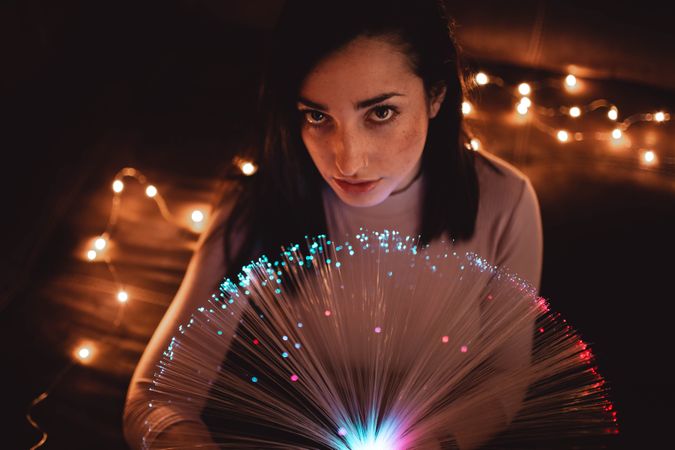 Young woman with fairy lights in darkness