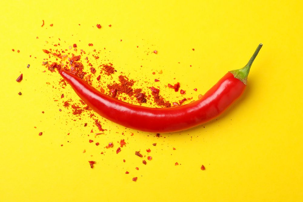 Tasty chilli pepper and powder spice on yellow background