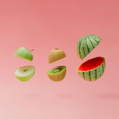 Watermelon, apple and kiwi halved on pastel pink background