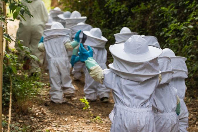Company of kids in protective costumes in apiary