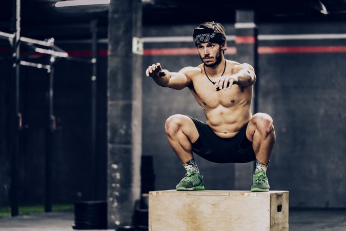 Athletic man jumping on box to improve stamina in gym
