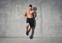 Shirtless muscular man leaning against grey wall