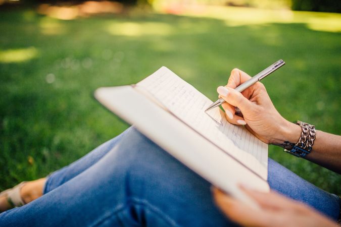 Cropped image of woman writing on a notebook sitting on green grass