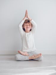 Boy in white pajamas leaning against the white wall of his house.