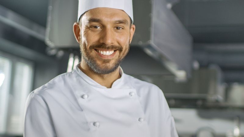Portrait of a Handsome Young Chef Smiling On Camera in Slow Motion. Shallow Depth of Field Shot.
