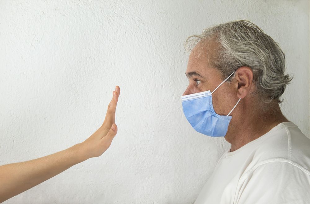 Side view of middle aged man with facemask being stopped by a hand against light background