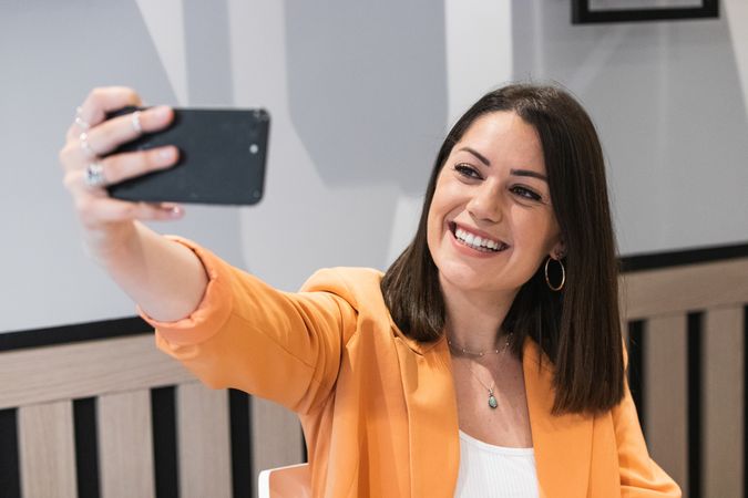 Cheerful woman taking selfie on smartphone in cafe