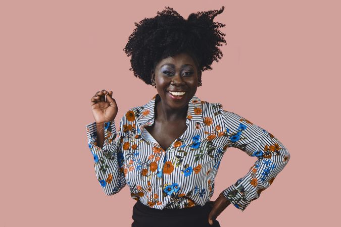 Studio shot of Black woman in floral print shirt with one hand up and one on her hip