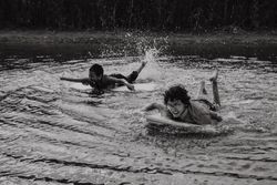 Happy boys swimming with board over water