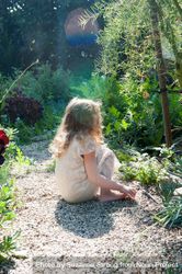 Side view of little girl sitting on pebble path in garden 0Ld1e0