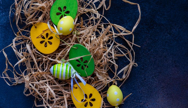 Easter decorations scattered in straw on navy table