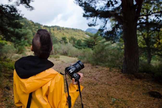 Enthusiastic person in yellow raincoat photographing tree in mountain
