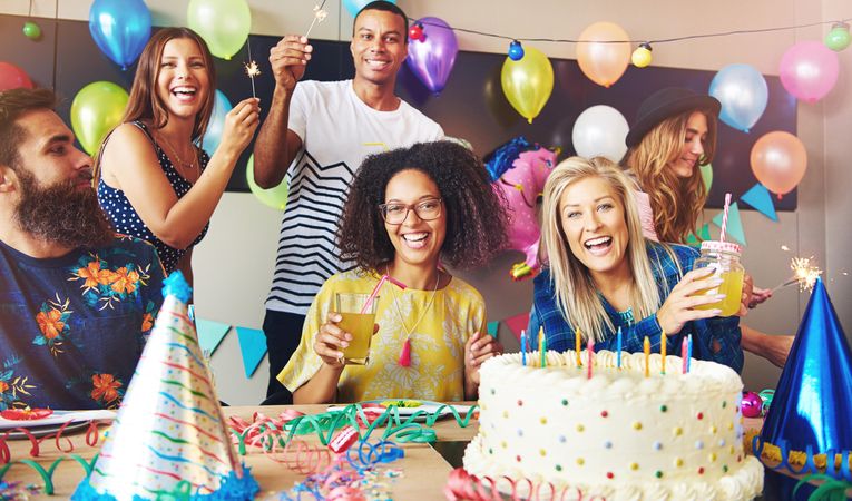 Smiling multi-ethnic friends lighting sparklers at birthday party with cake and balloons