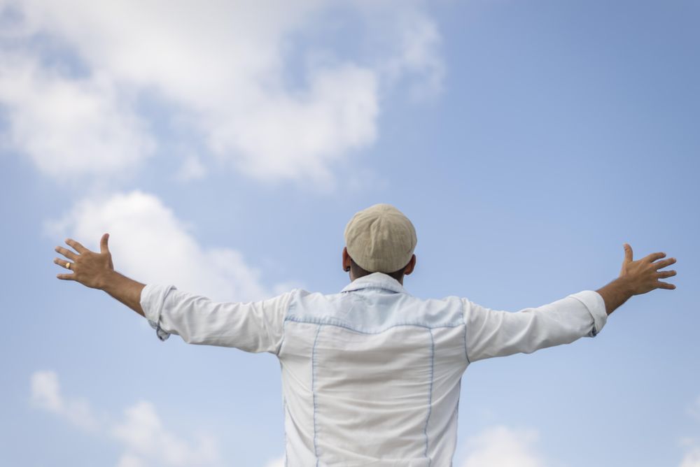 Male in denim standing with outstretched arms on sunny day