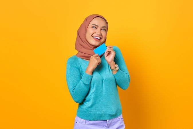 Muslim woman smiling while holding credit card with both hands