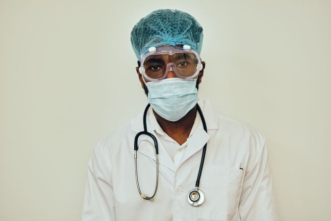 Portrait of Black male doctor in bright studio with ppe gear ready for procedure, vertical