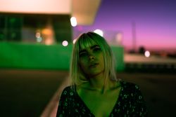 pensive adult woman looking at camera against vibrant sky at dusk