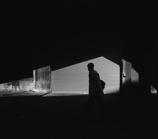 Man walking through shadows in front of garage door on street in stark minimalist shot