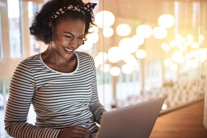 Woman smiling while working on her laptop on the second story looking out over lights