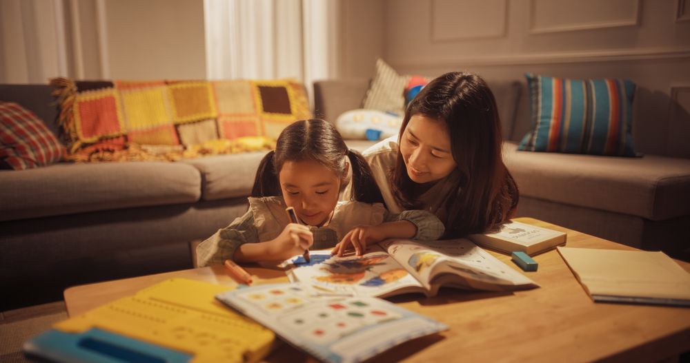 Portrait of Korean Mother Teaching her Little Daughter How to Draw in the Living Room at Home.