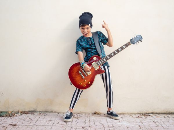 Energetic kid gesturing rock holding guitar