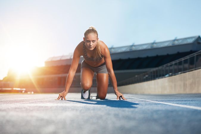 Confident young female athlete in starting position ready to start a sprint