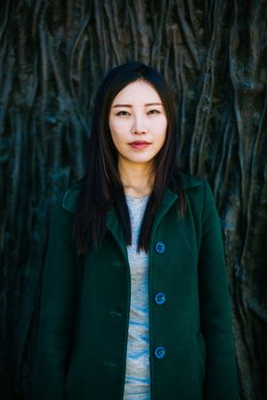 Pensive Asian woman leaning on rough wall