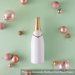 Champagne bottle and Christmas baubles on light green surface 4AlAm5