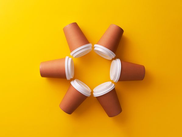 Disposable coffee cups on yellow background in circle shape