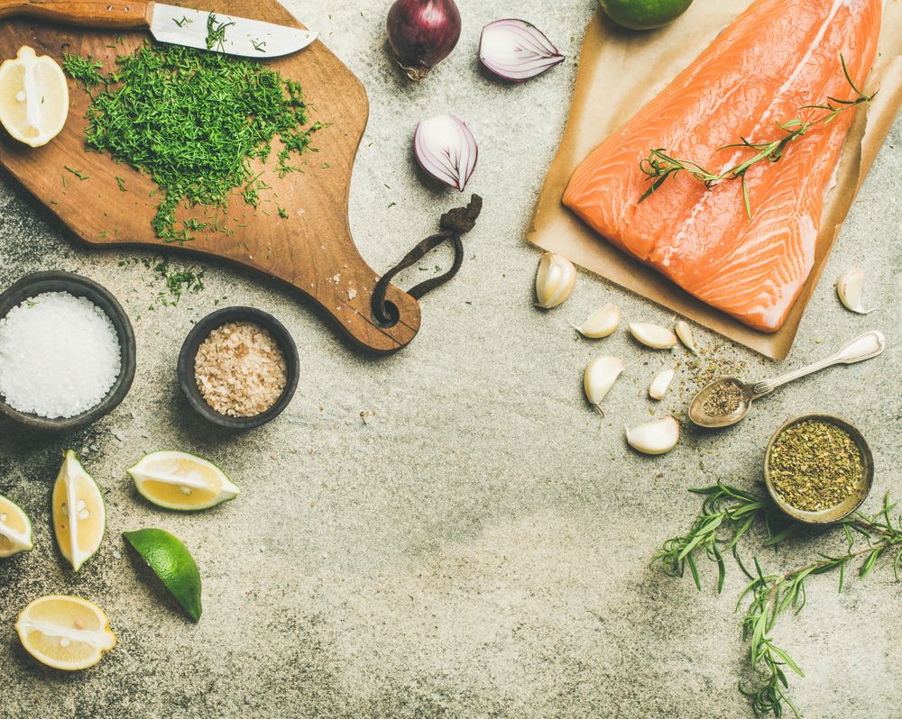 Salted salmon fillet with fresh herbs, limes, onions, bread board, copy space