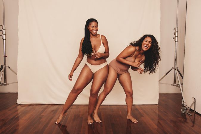 Two happy young women laughing and dancing while wearing underwear