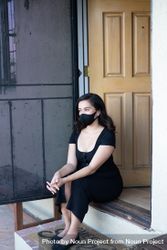 Woman sitting by front door of house with mask 5lVyMb