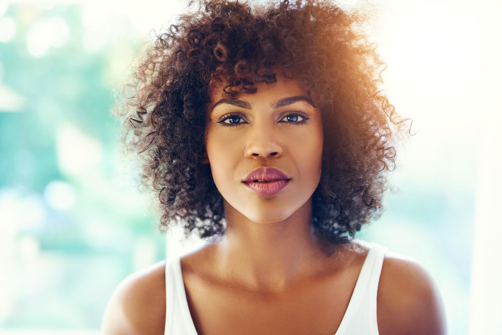 Serious female looking at camera with curly hair on leafy background