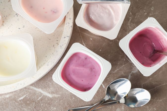 Composition with plastic cups with yogurt on grey table