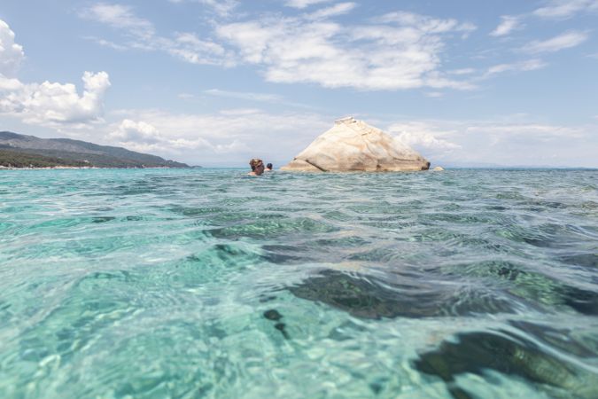 Travelers near big rock in clear water